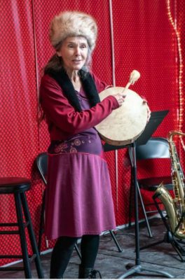Storyteller in red dress with fur hat and drum