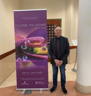 Bill Boxer standing to the right of his Close to Home exhibition banner at the Rotunda Gallery.
