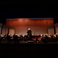 Gallery 1 - A full orchestra performs on a stage with warm lighting