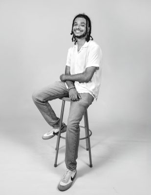 Artist Brandon Santiago poses on stool.