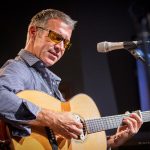 Gallery 1 - Sam Pacetti playing acoustic guitar on stage.